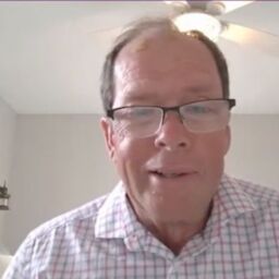 Greg Ritscher looks handsome in front of a white room. He is a middle-aged white man in a button down, plaid shirt.