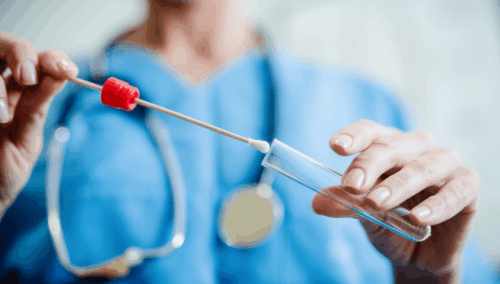 genetic testing for Young Onset Parkinson's. This is a headless woman who is putting a swab into a test tube. She is wearing blue scrubs and a stethoscope.