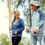 A young adult walks in a park with an older person.